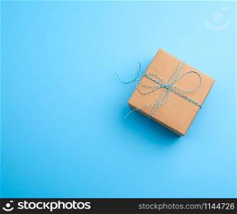 closed brown square box with a gift tied rope on a blue background, top view, empty place for an inscription