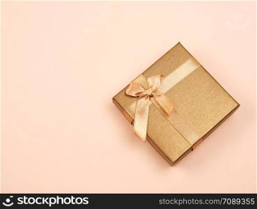 closed golden gift box with a bow on a beige background, top view, festive backdrop