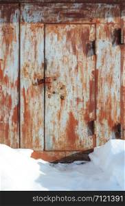Closed old rusty metal garage gate, narrow footpath in snow