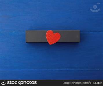 closed rectangular cardboard box with a gift, red paper heart from above, blue wooden background from boards, top view