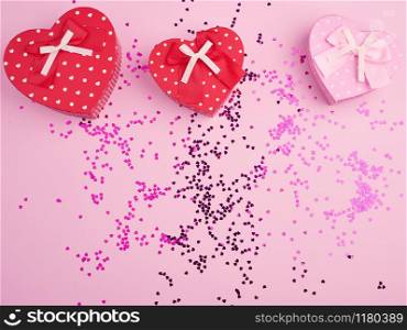 closed red and pink heart-shaped cardboard boxes on a pink background with multi-colored shiny confetti, festive backdrop for birthday, Valentine&rsquo;s day