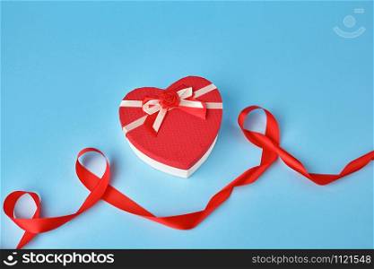 closed red heart-shaped gift box with a bow on a blue background, top view, festive backdrop. Valentine gift
