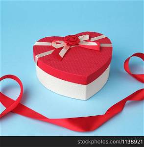 closed red heart-shaped gift box with a bow on a blue background, top view, festive backdrop. Valentine gift
