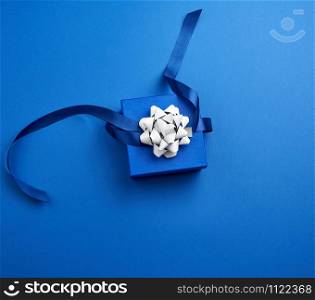 closed square blue box with a gift tied with a blue ribbon with a bow on a blue classic background, top view, trend color