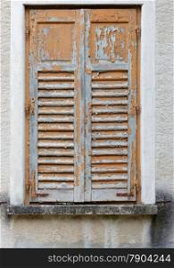 Closed window of the old building covered by wooden blinds with peeling paint
