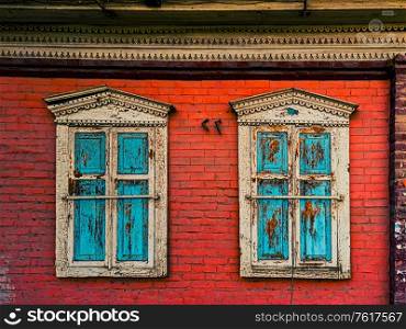 Closed wooden shutters on the windows in the red brick wall of the house