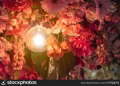 Closeup a light bulb with artificial flowers hanging from ceiling. Wedding floral decoration concept.