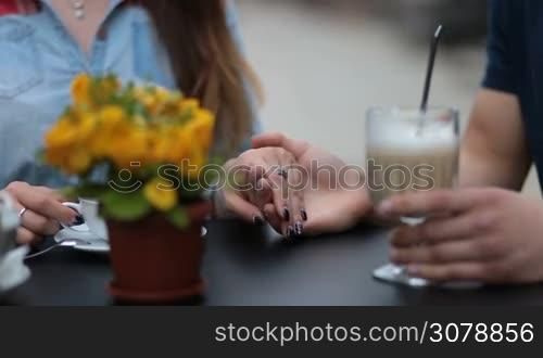 Closeup affectionate couple holding hands in sidewalk cafe. Male hands caressing fingers of his beloved woman with tenderness and love while couple sitting at the table in open air coffee shop during romantic date.