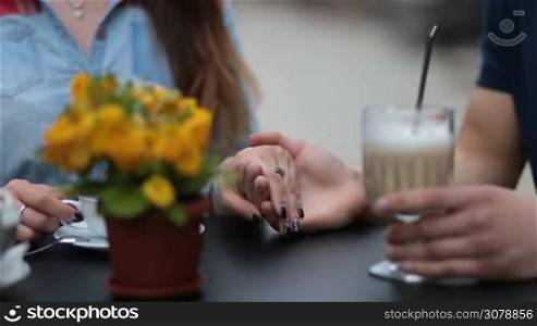 Closeup affectionate couple holding hands in sidewalk cafe. Male hands caressing fingers of his beloved woman with tenderness and love while couple sitting at the table in open air coffee shop during romantic date.