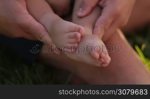 Closeup affectionate father holding tiny infant child&acute;s feet in his hands. Caring daddy rubbing small baby boy feet with his hands. Love, tenderness and care concept.