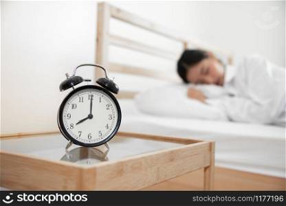Closeup alarm clock with sleeping woman in bed room. Lazy time in holiday concept.
