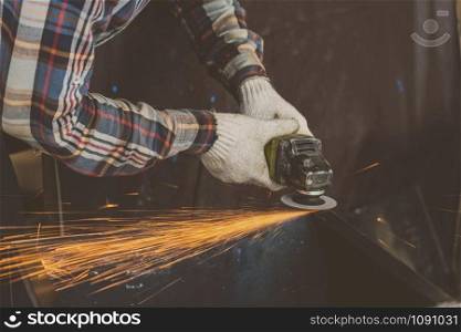 Closeup angle Grinder hand holding and Grinding the spare parts of metal over the wooden table in metal factory, industry concept