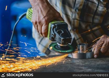 Closeup angle Grinder hand holding and Grinding the spare parts of metal over the wooden table in metal factory, industry concept