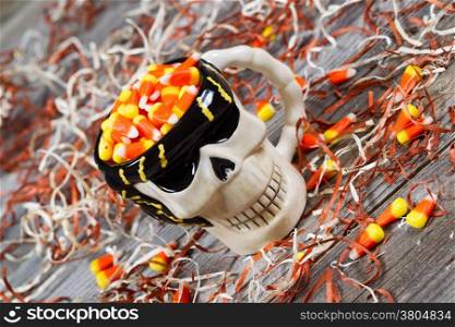Closeup angled horizontal image of a scary black and white skeleton skull cup surround by shredded paper, candy and rustic wooden boards