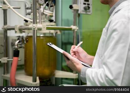 Closeup apothecary scientist using a clipboard and pen to record information from a CBD oil extractor and a scientific machine used to create medicinal cannabis products.. Closeup apothecary scientist recording data from CBD oil extractor in laboratory