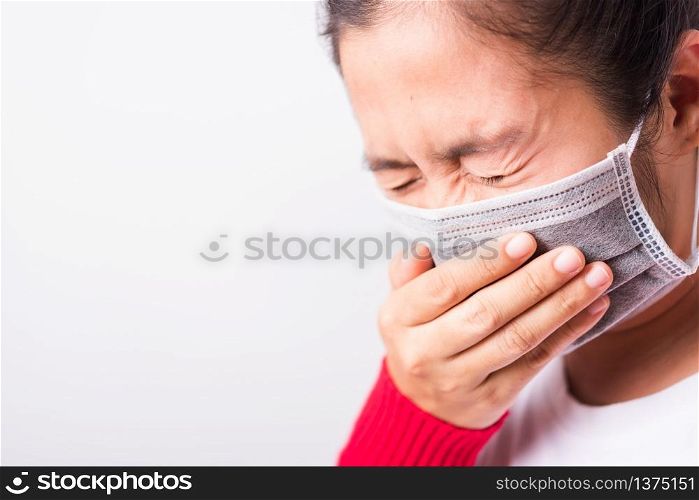 Closeup Asian adult woman wearing red shirt and face mask protective against coronavirus or COVID-19 virus or filter dust, air pollution her sneezing use hand close mouth, isolated white background