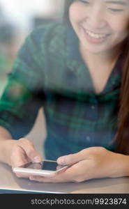 Closeup Asian businesswoman hand using the smart mobile phone with happiness action on the desk beside the glass in workplace or co-working space or modern office, business lifestyle concept