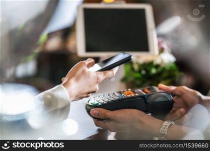Closeup Asian customer man hand paying money via contactless channel by mobile banking application to Small business owner at table in cafe shop, Small business owner and startup in coffee shop