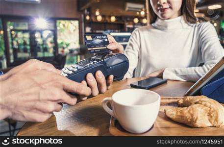 Closeup Asian customer woman paying with credit card via contactless nfs technology to Asian Small Coffee shop owner at the female table in cafe,Small business owner and startup in coffee shop concept