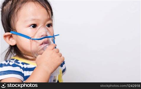 Closeup Asian face, Little baby girl sick her using steam inhaler nebulizer mask inhalation oneself on white background with copy space, health medical care