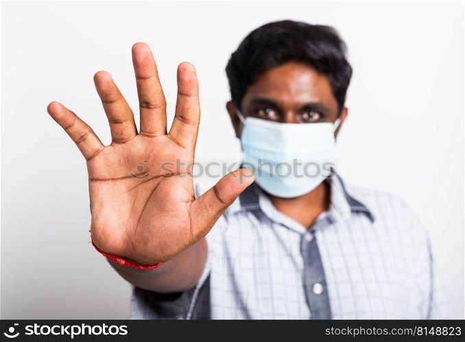 Closeup Asian handsome black man wearing surgical hygienic protective cloth face mask against coronavirus and raising hand stop sign, studio shot isolated white background, COVID-19 medical concept