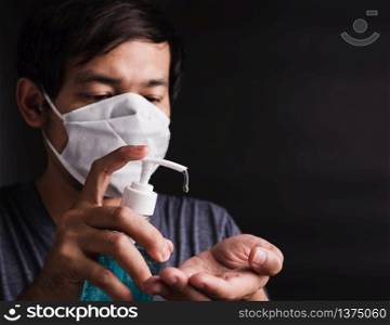 Closeup Asian handsome man wearing protective face mask fear in eye holding show sanitizer gel near face, hygiene prevention COVID-19 virus or coronavirus protection concept dark on black background