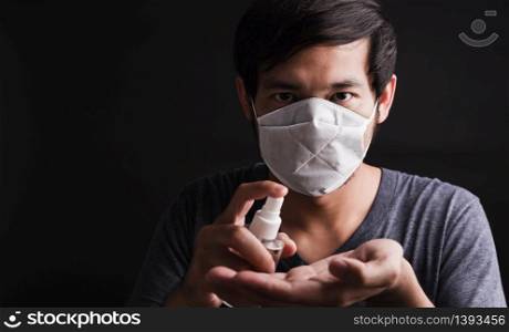 Closeup Asian handsome man wearing protective face mask fear in eye holding show sanitizer spray near face, hygiene prevention COVID-19 virus or coronavirus protection concept dark on black background