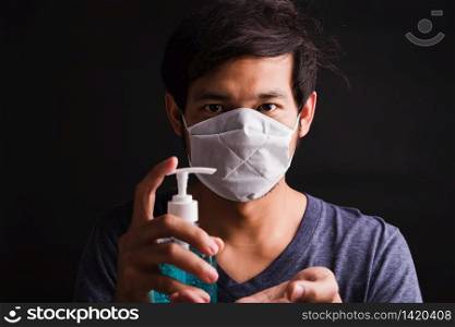 Closeup Asian handsome man wearing protective face mask fear in eye holding show sanitizer gel near face, hygiene prevention COVID-19 virus or coronavirus protection concept dark on black background