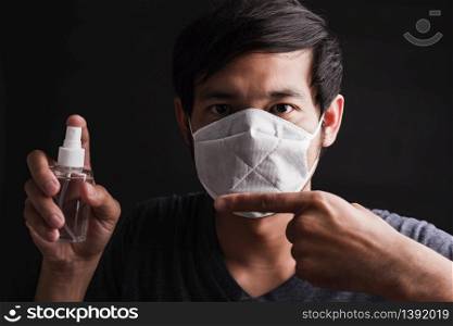 Closeup Asian handsome man wearing protective face mask with fear in eye holding and point sanitizer spray, hygiene prevention COVID-19 virus or coronavirus protection concept dark on black background