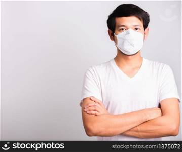 Closeup Asian handsome Man wearing surgical hygienic protective cloth face mask against coronavirus and stand crossed arm, studio shot isolated white background, COVID-19 medical concept