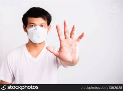 Closeup Asian handsome Man wearing surgical hygienic protective cloth face mask against coronavirus and raising hand stop sign, studio shot isolated white background, COVID-19 medical concept