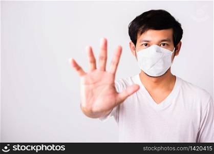 Closeup Asian handsome Man wearing surgical hygienic protective cloth face mask against coronavirus and raising hand stop sign, studio shot isolated white background, COVID-19 medical concept