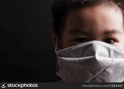 Closeup Asian little child wearing protective face mask with fear in the eye, prevent germs or disease hygiene prevention COVID-19 virus or coronavirus protection concept, dark on black background