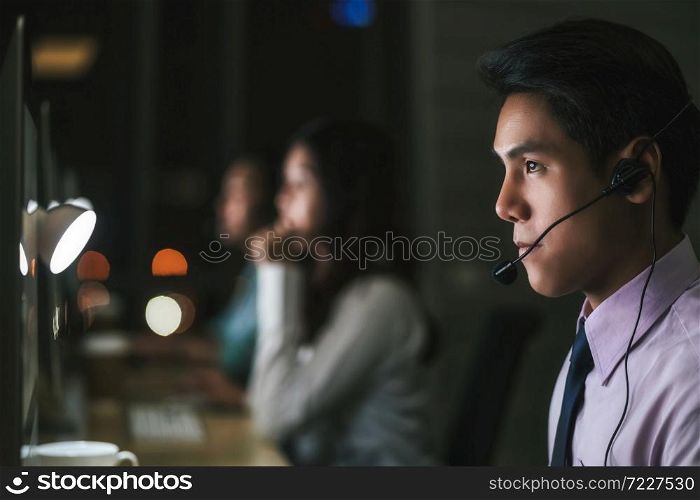 Closeup Asian Male customer care service over business woman working hard late in night shift at office,call center department,worker and overtime,team work with colleagues for success, 7 day 24 hour