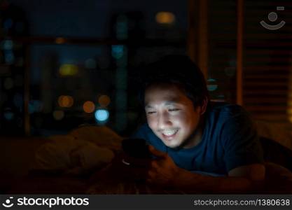 Closeup Asian man sleeping and using smart mobile phone for social network or video conference call and face time to her lovers on bed over blur city at night time, lifestyle and relax, work from home