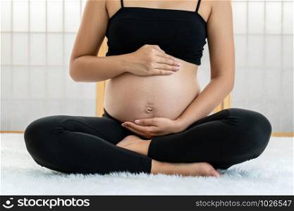 Closeup Asian Pregnant sitting and holds hands on belly in japanese style house on the white carpet, pregnant concept, preparing to be motherhood with good healthy