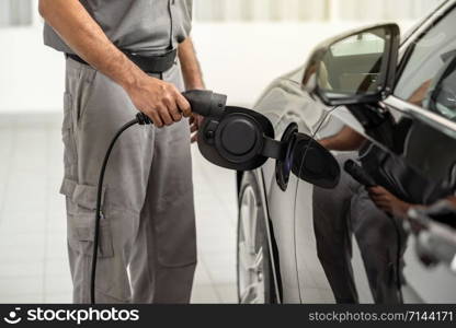 Closeup asian Technician hand is charging the electric car or EV in service center for maintainance, Eco-friendly alternative energy concept