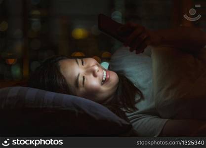 Closeup Asian woman sleeping and using smart mobile phone for social network or video conference call and face time to her lovers on bed over blurred city at night time, lifestyle and relax concept