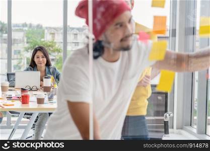 Closeup Asian woman working which have photo blurred of creative writing and pointing the postit on the millor board when presenting the ideas in the modern workplace