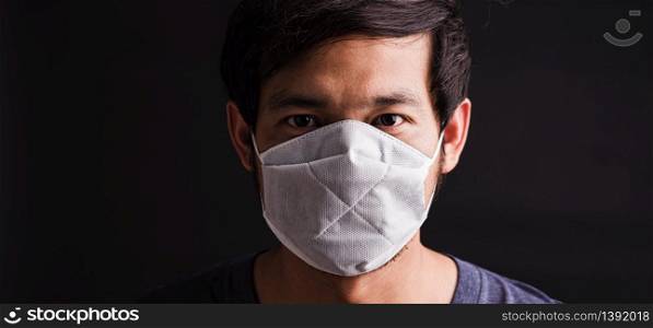Closeup Asian young man wearing protective face mask with fear in the eye, prevent germs or disease hygiene prevention COVID-19 virus or coronavirus protection concept, dark on black background