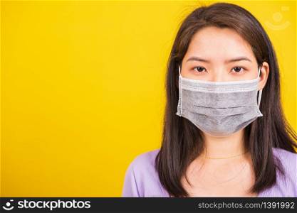 Closeup Asian young teen woman wearing face mask protective against coronavirus, COVID-19 virus or filter dust pm2.5 and air pollution she looking camera studio shot isolated yellow background