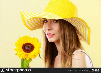 Closeup attractive summer woman in straw hat with sunflower in her hand on yellow background