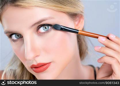 Closeup beautiful girl with flawless applying alluring eye shadow makeup with eyeliner brush. Cosmetic facial painting process on lovely young woman with perfect clean skin on isolated background.. Closeup beautiful girl with flawless applying alluring eye shadow makeup.