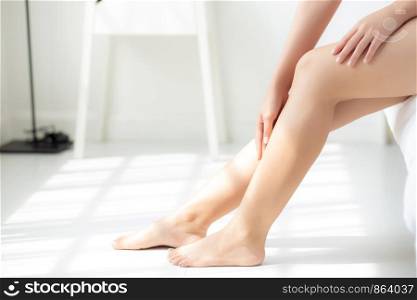 Closeup beautiful young asian woman sitting on a bed stroking legs with soft smooth skin in the bedroom, girl applying body cream and lotion with treatment care, healthy and wellness concept.