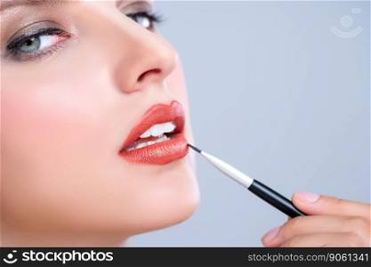 Closeup beautiful young woman with flawless healthy skin and natural makeup putting alluring fashion glossy red lipstick on her lip with lip brush in isolated background.. Closeup beautiful young woman putting alluring fashion glossy red lipstick.