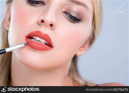 Closeup beautiful young woman with flawless healthy skin and natural makeup putting alluring fashion glossy red lipstick on her lip with lip brush in isolated background.. Closeup beautiful young woman putting alluring fashion glossy red lipstick.