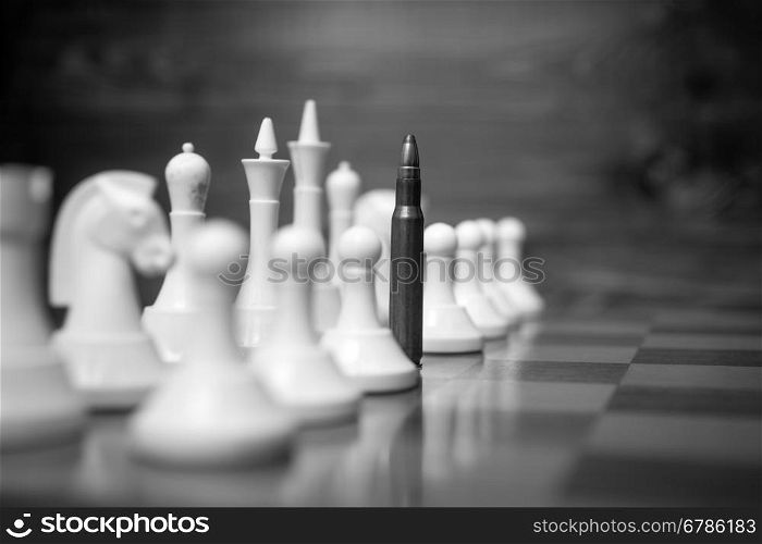 Closeup black and white conceptual photo of riffle bullet on chessboard