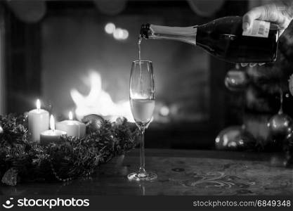 Closeup black and white image of champagne flute being filled from bottle on Christmas