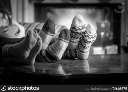 Closeup black and white photo family wearing woolen socks warming at fireplace