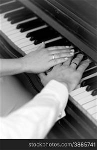 Closeup black and white photo of bride and groom playing on piano